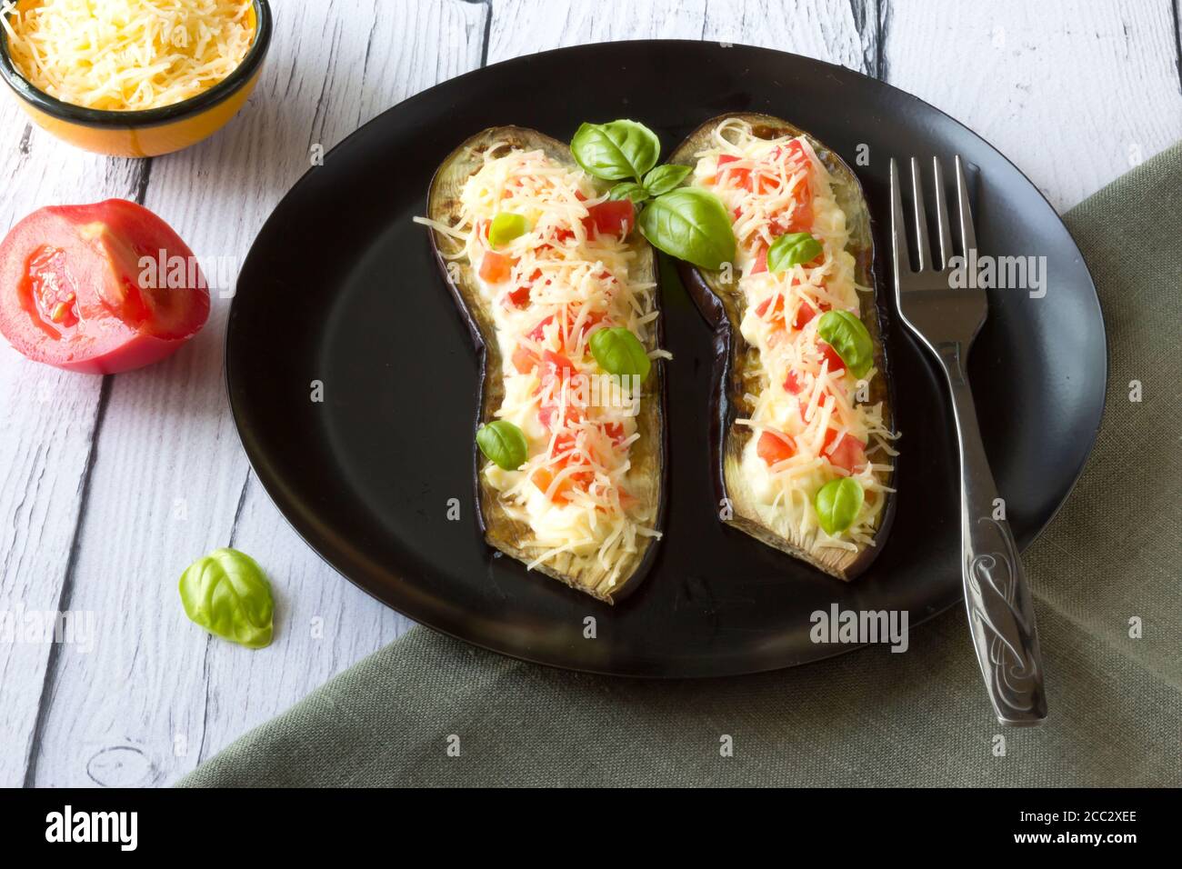 Eggplant stuffed with tomatoes, grated cheese and cranberries, garnished with Basil on a dark plate over gray slate Stock Photo