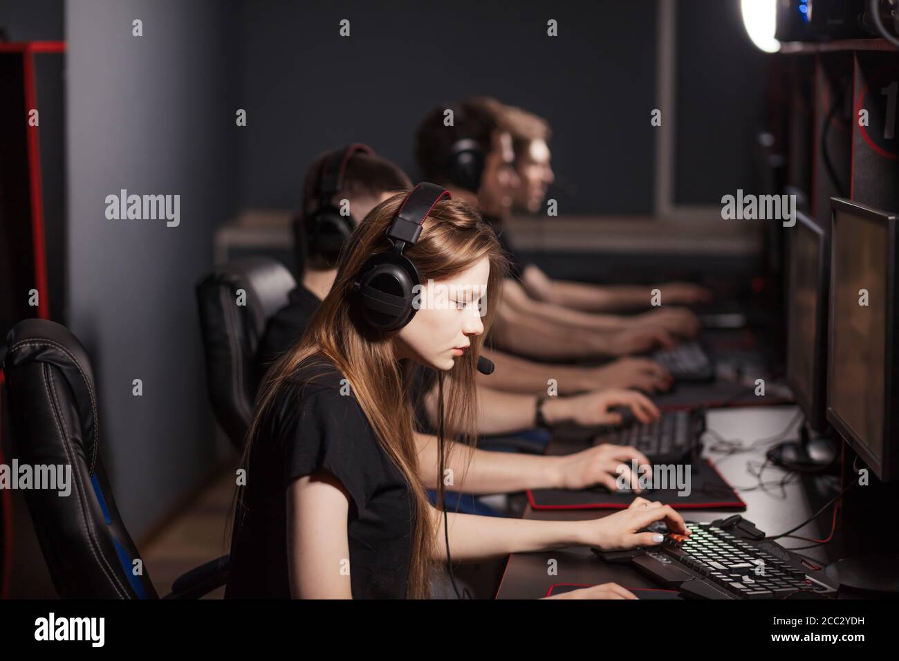 A cute female gamer girl with headset sits in a dark room behind a