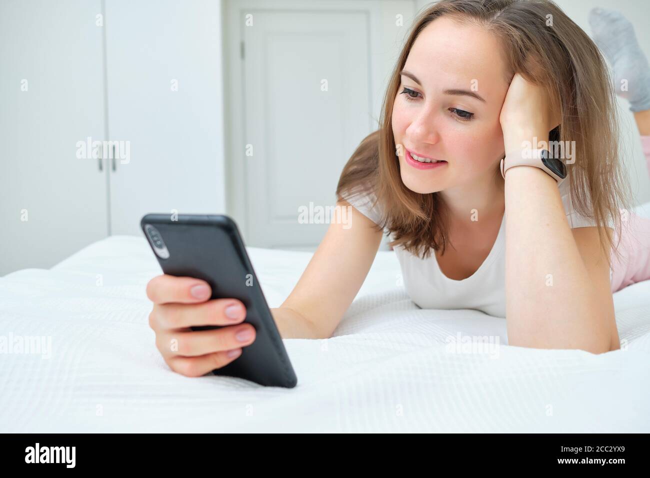 Beautiful young woman lying on the bed and looking at her smartphone Stock Photo