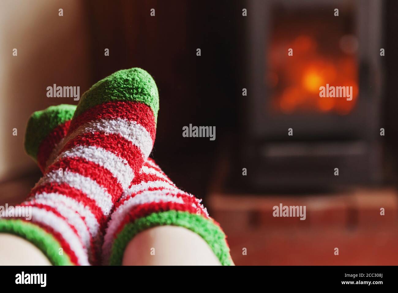 Feet legs in winter clothes wool socks at fireplace background. Woman sitting at home on winter or autumn evening relaxing and warming up. Winter and cold weather concept. Hygge Christmas eve Stock Photo