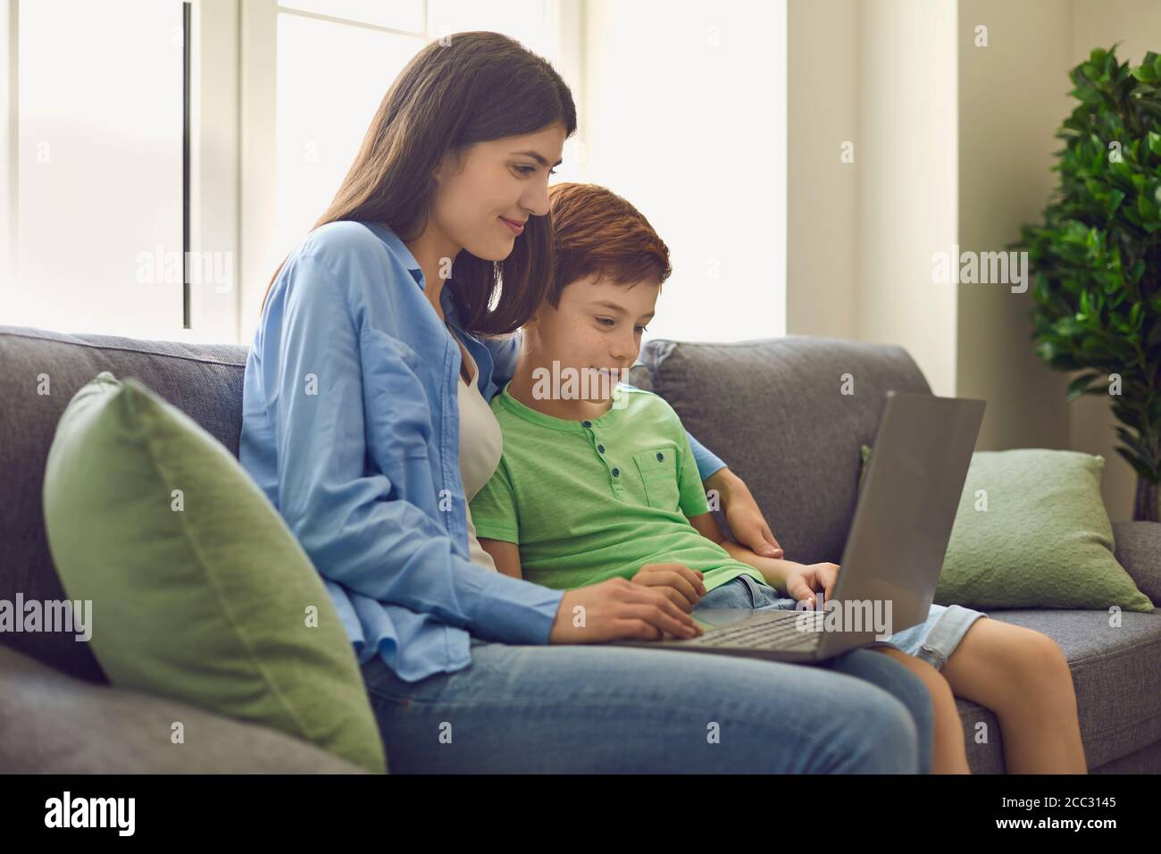 Young mother and her son talking to teacher from home. Parent and child watching online lesson on laptop computer Stock Photo