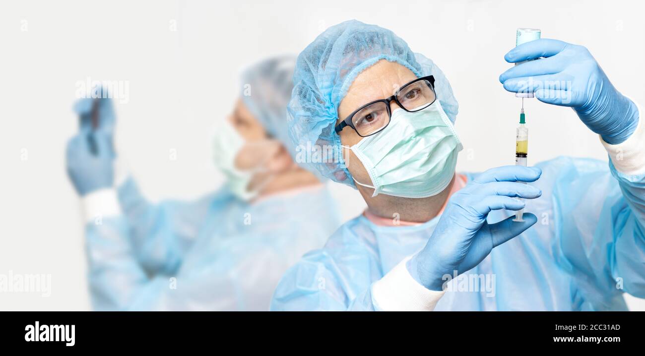 The doctor takes the medication from a bottle to an injection, on a background a coworker. Team of scientists research the vaccine. Stock Photo
