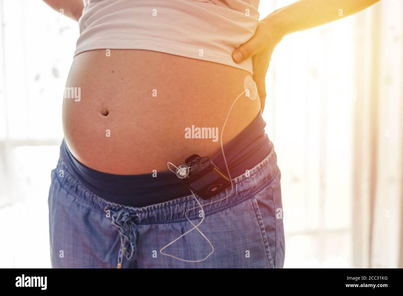 Pregnant woman with insuline pump on her pants and drainage mounted on her belly. Modern