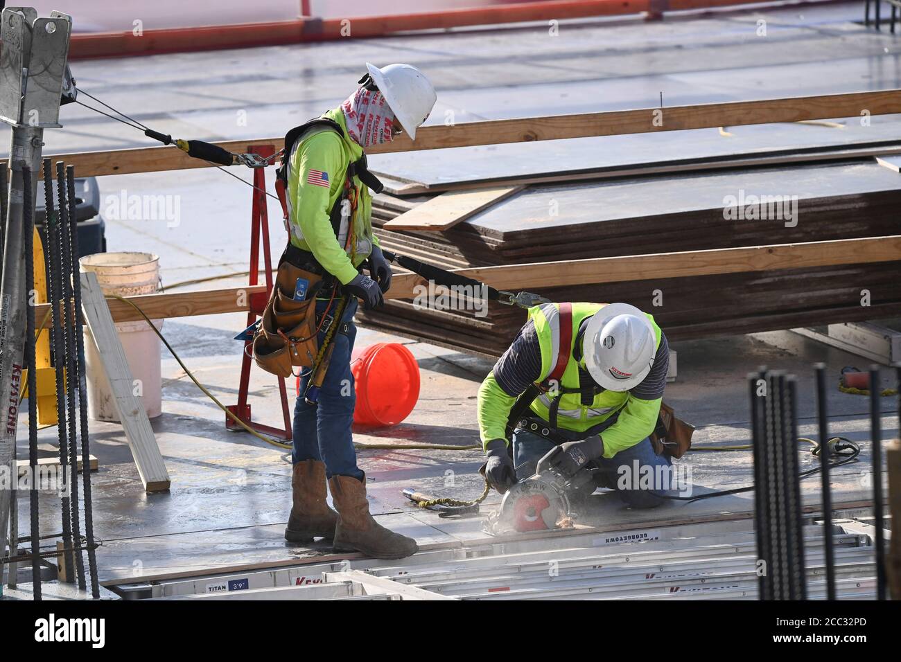 Construction workers wearing safety gear and face coverings team up on job site of parking garage in Rainey Street district near downtown Austin, Texas. Stock Photo