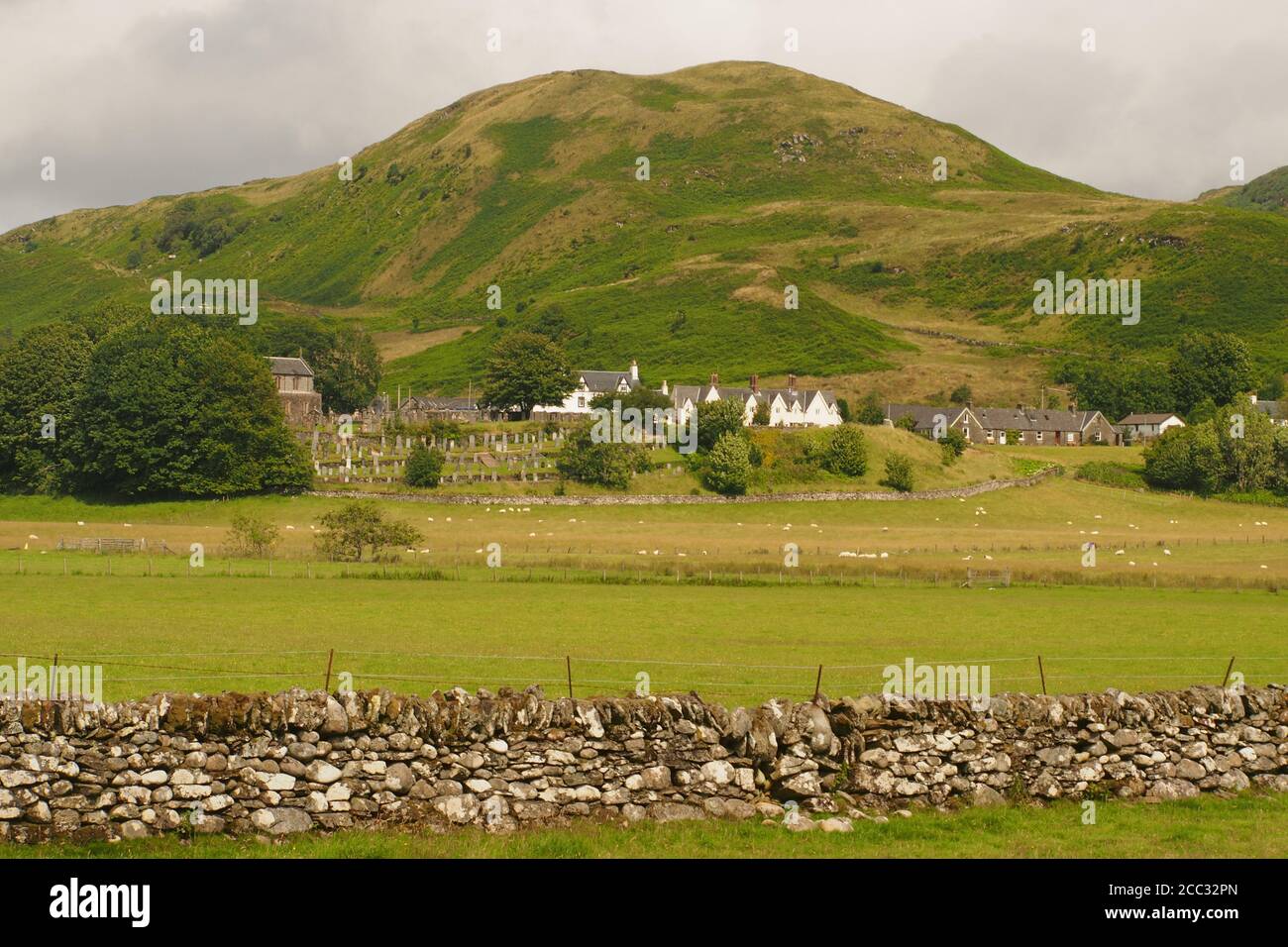 A view of Kilmartin chuch, hotel and houses from Kilmartin Glen with Barr Mor rising up behind and a dry stone wall in the foreground Stock Photo