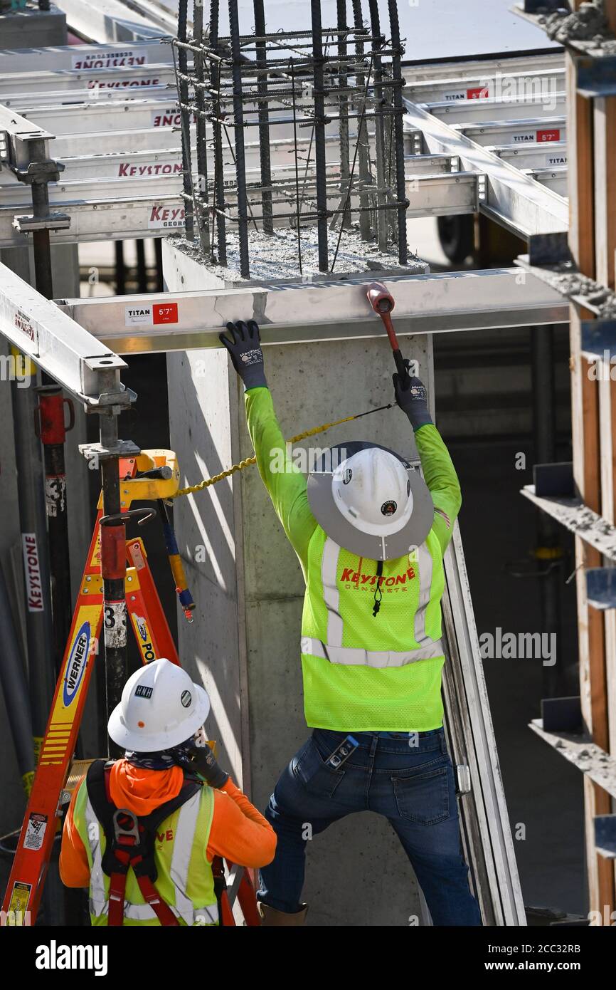 Construction workers wearing safety gear and face coverings team up on job site of parking garage in Rainey Street district near downtown Austin, Texas. Stock Photo