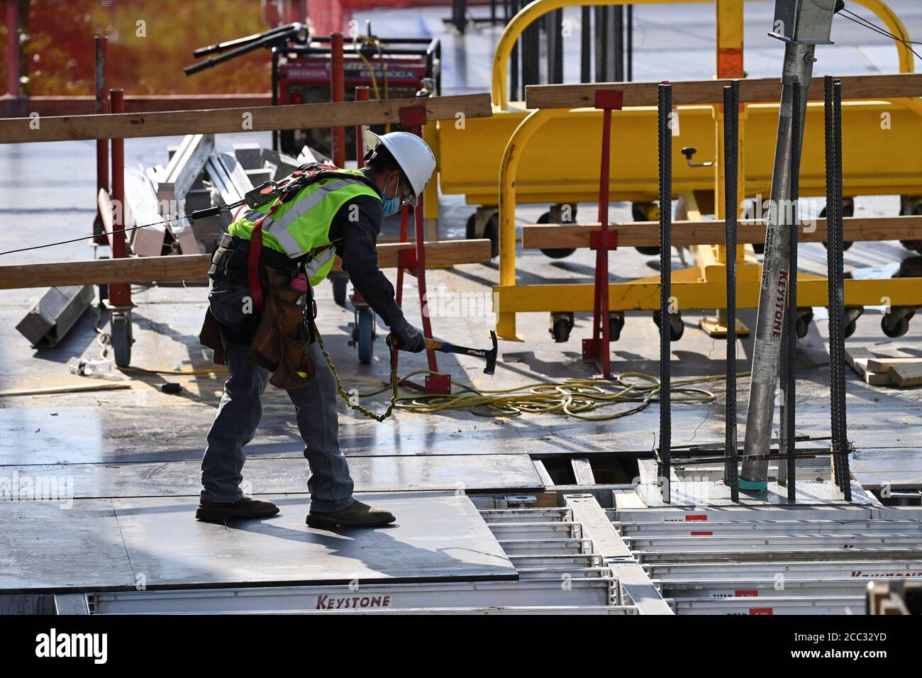Construction worker wearing safety gear and face covering uses hammer