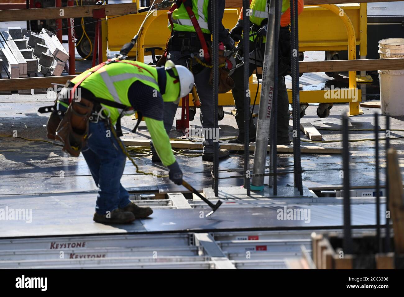 Construction worker wearing safety gear and face covering uses hammer