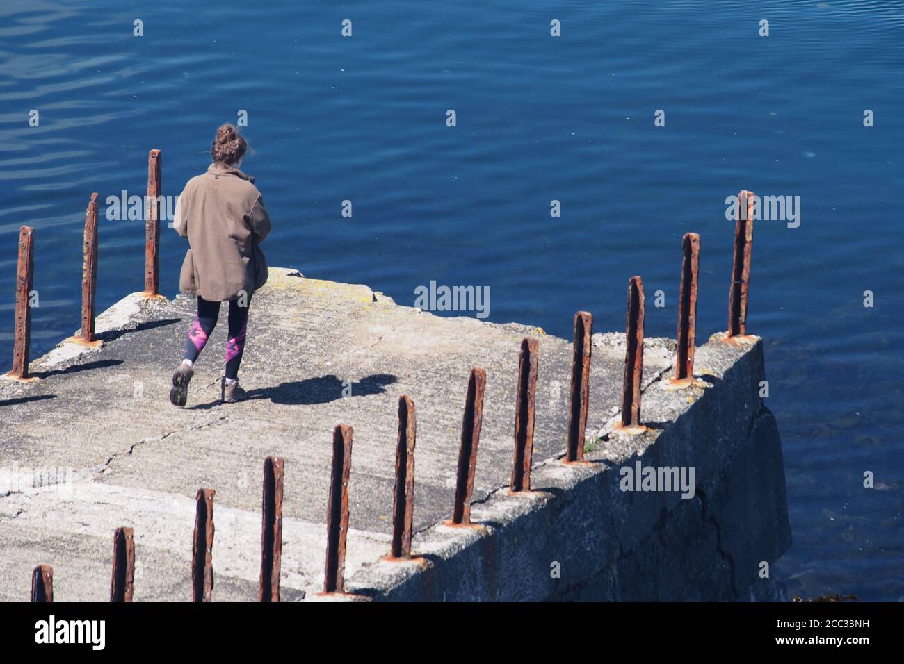 A young woman standing alone on a broken pier looking out to sea into the Sound of Jura from the Craignish penisula, Argyll,Scotland Stock Photo