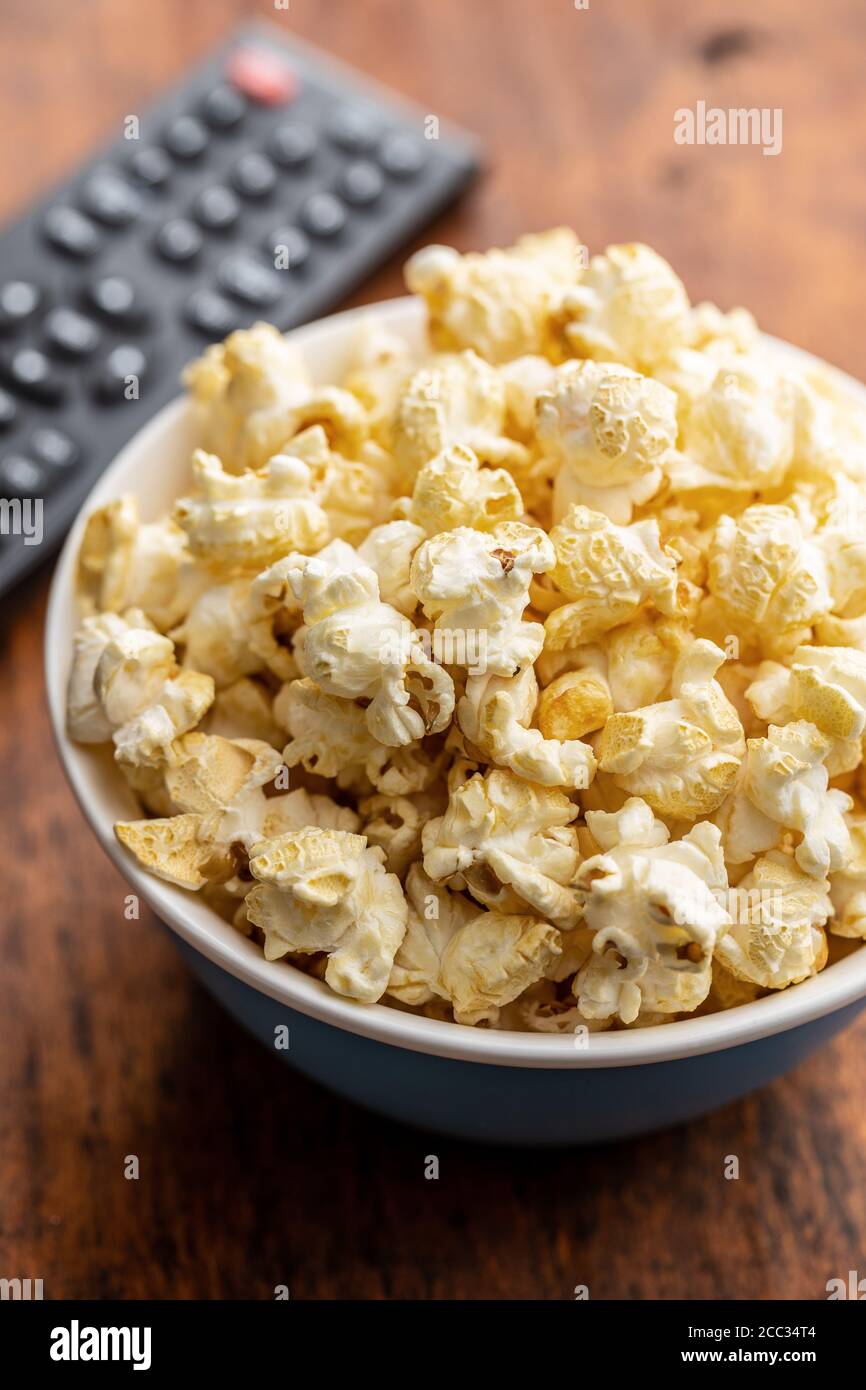 Sweet tasty popcorn in bowl and TV remote control on wooden table. Stock Photo