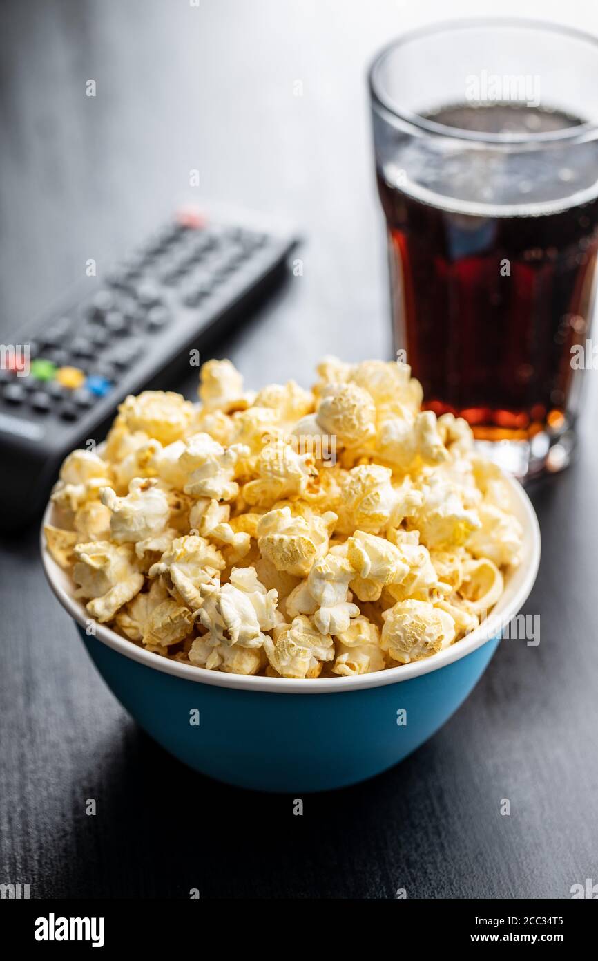 Sweet tasty popcorn in bowl and TV remote control on black table. Stock Photo