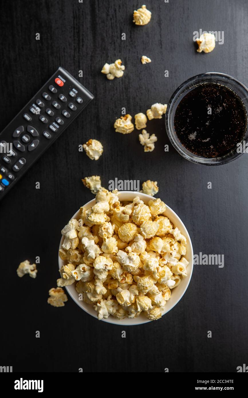 Sweet tasty popcorn in bowl and TV remote control on black table. Top view. Stock Photo