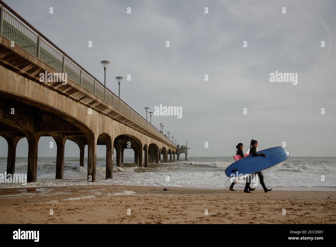 two woman with surf boards on Bournemouth beach Stock Photo