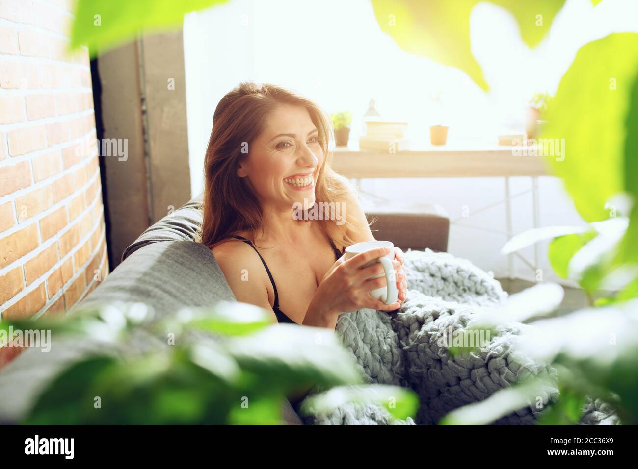 Brunette girl drinking cappuccino for breakfast on a sofa. Concept of relax. Stock Photo