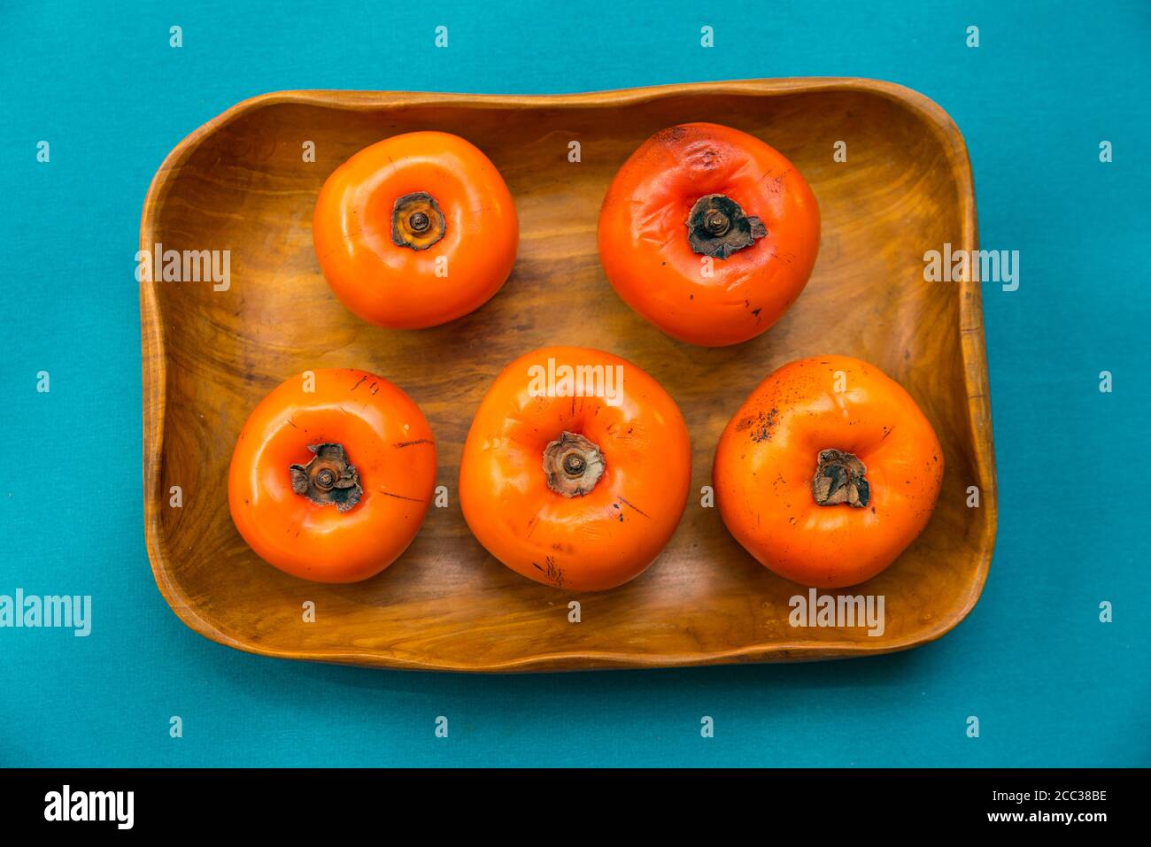 Top view of persimmon fruits in a wood bowl and a blue background. Stock Photo