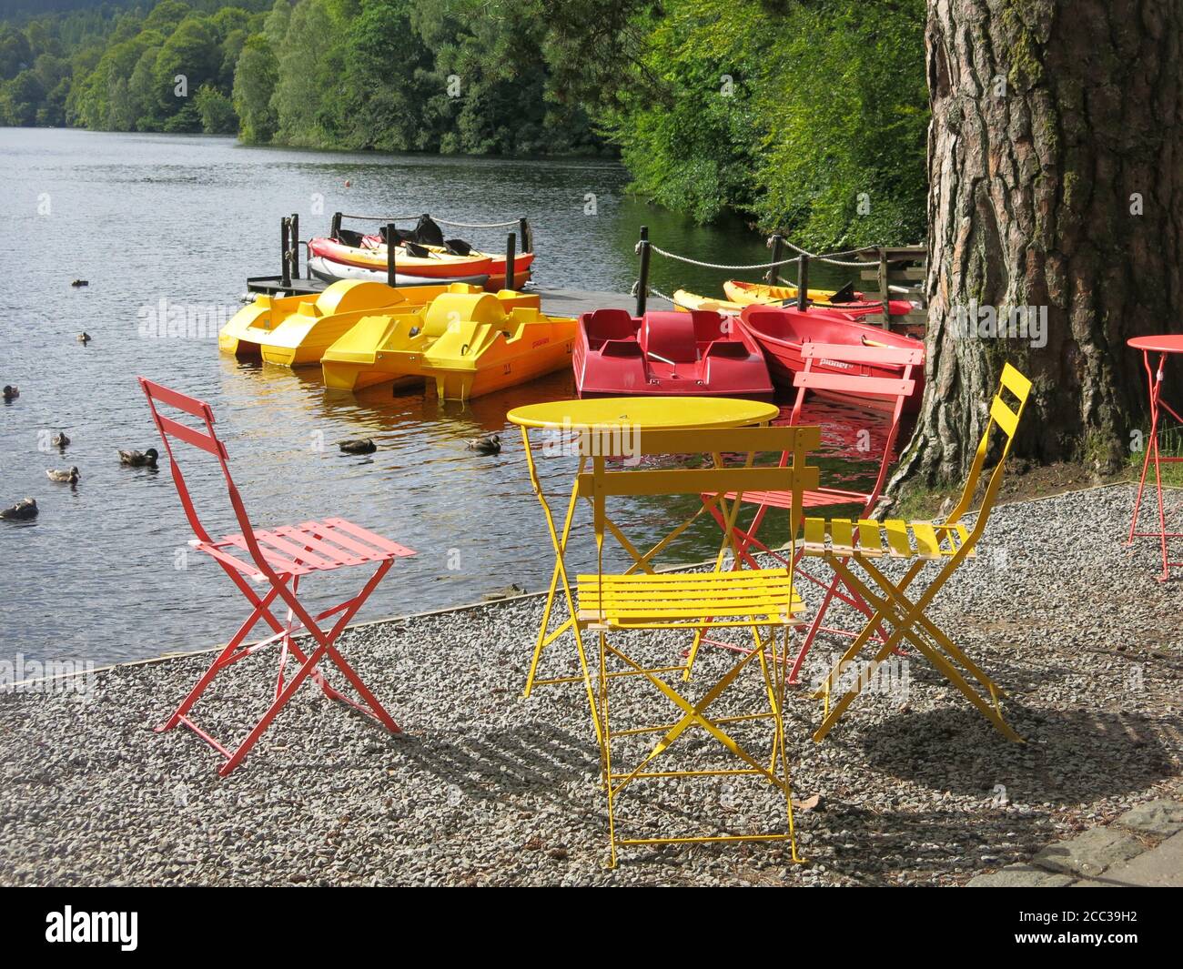Colourful scene of red and yellow bistro table and chairs to match the pedalos for hire at the Pitlochry Boating Station on Loch Faskally. Stock Photo