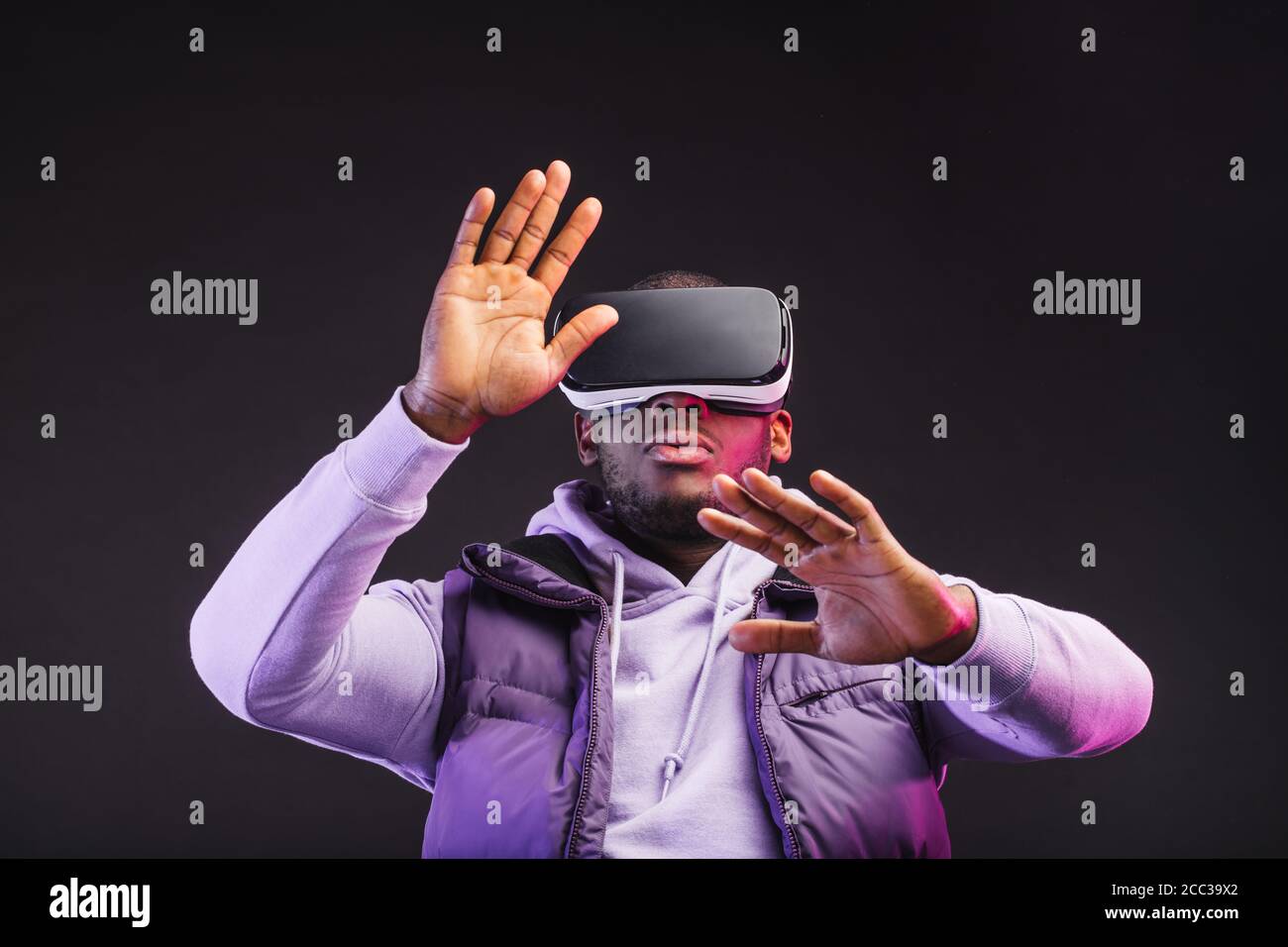 Young dark-skinned man dressed in outdoor wear having on head mobile virtual reality headset for playing 3D game but Mankind meets a new era of contro Stock Photo
