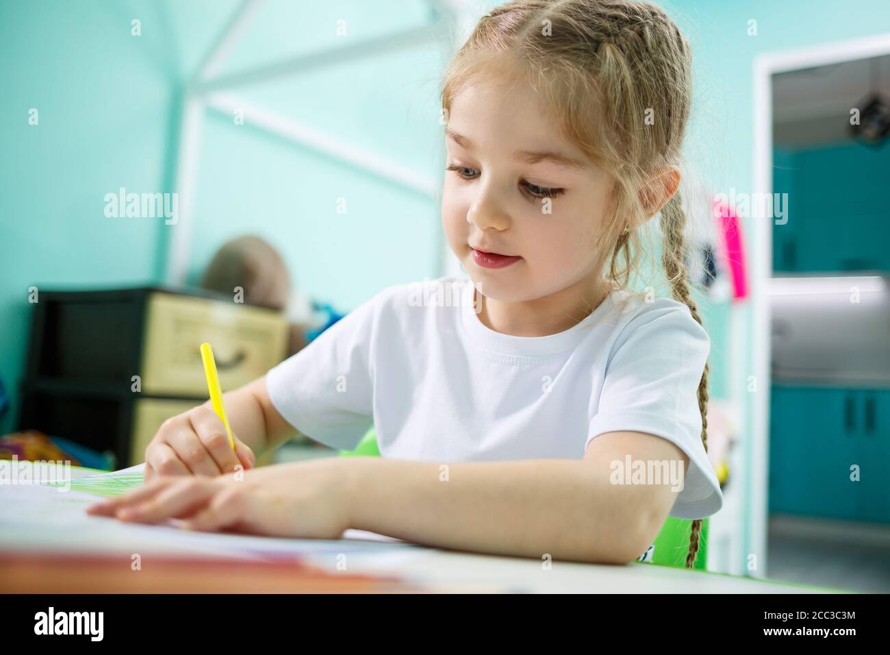 Adorable toddler girl drawing with pencils at home sitting at the table. Creative child sitting in a room learning to draw. Toddler girl doing Stock Photo