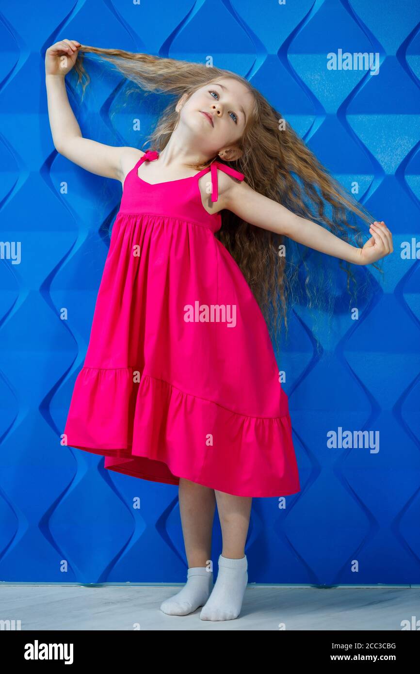 Little girl with long curly hair in a pink dress on a blue background  dances and laughs, bright children's emotions of joy, happy childhood Stock  Photo - Alamy