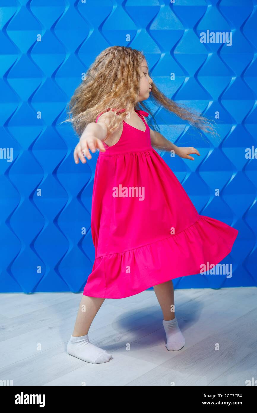 Little girl with long curly hair in a pink dress on a blue background ...