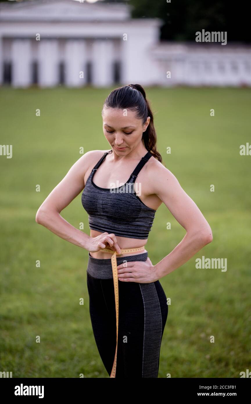 Beautiful young woman, while wearing a tight sports outfit, measures her  waist after doing pilates or yoga exercises Stock Photo - Alamy
