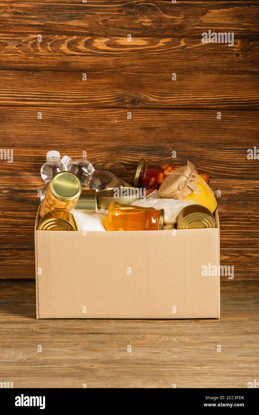 cardboard box with donated food on wooden background, charity concept