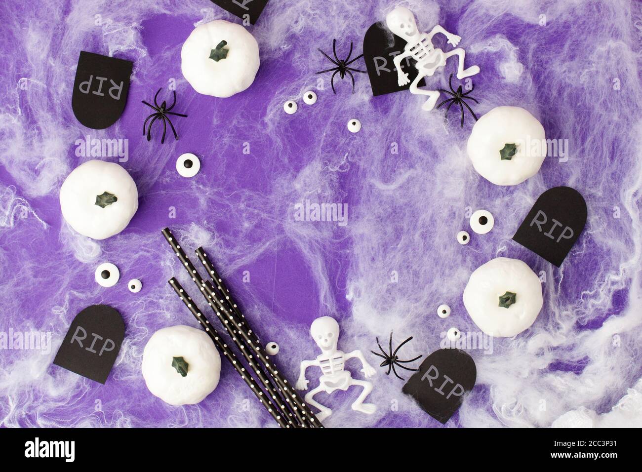 Halloween holiday blank with party decor, black spiders, white pumpkins, skeletons, eadstone rip, eyes, web on traditional purple. Flat lay, top view. Stock Photo