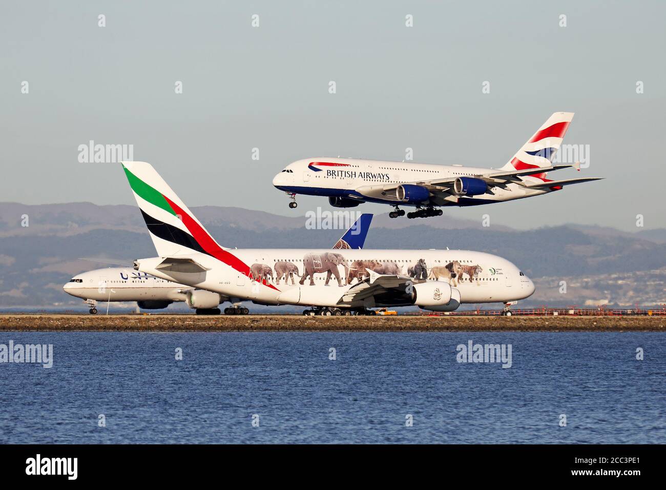 British Airways Airbus A380 arrives at San Francisco as an Emirates Airbus A380 waits for a United Airlines Boeing 777 to depart. Stock Photo