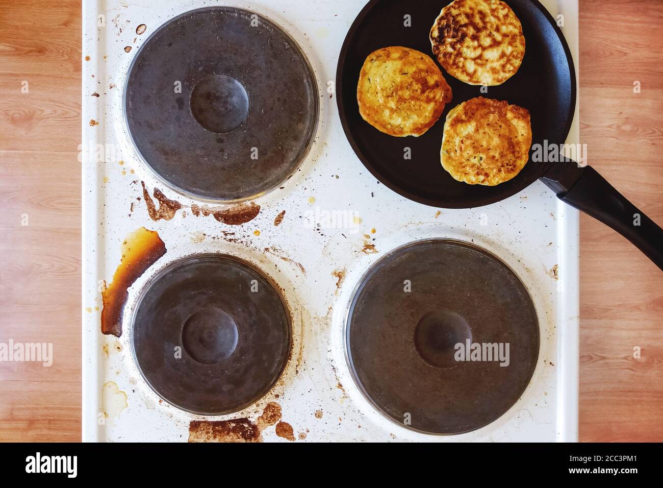 dirty kitchen stove with stains of burnt food and fat, frying pan with pancakes on top Stock Photo