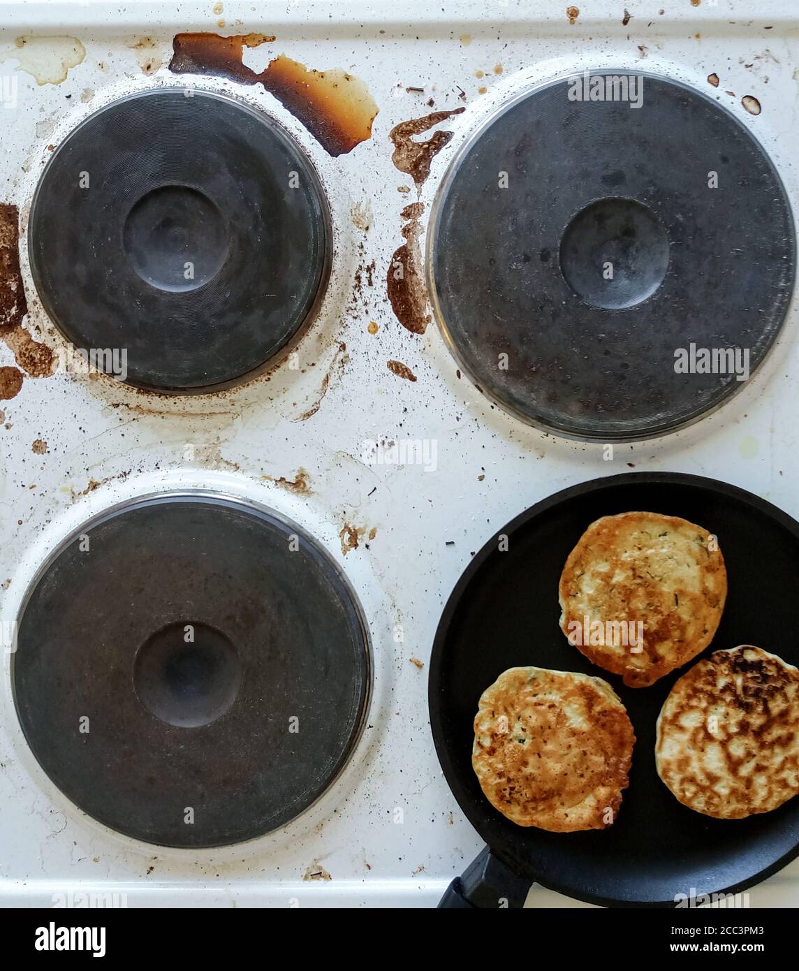 kitchen stove dirty with burnt food and cooking oil, frying pan with pancakes on top Stock Photo