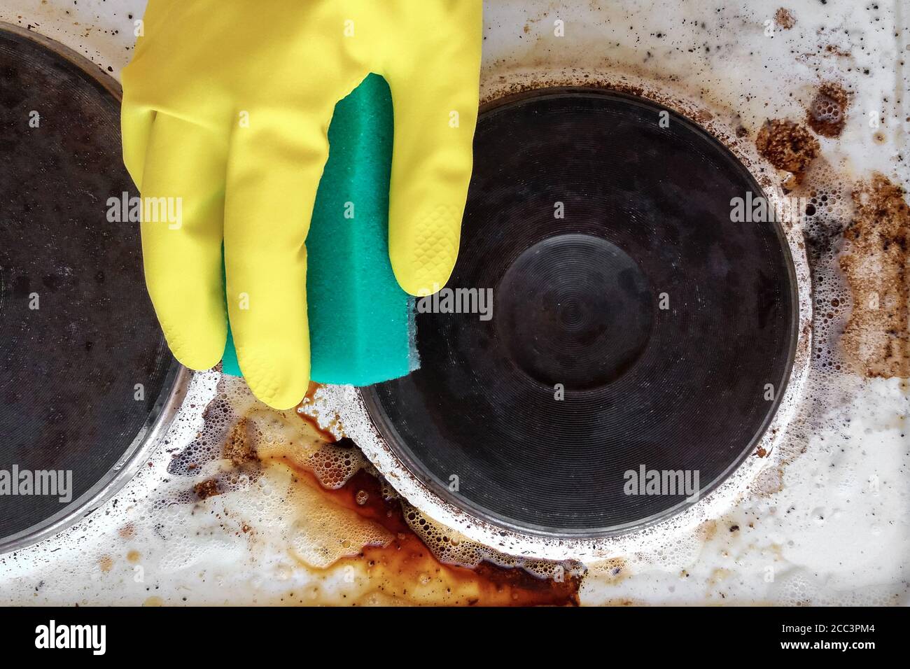 hand in household glove cleaning grease and dirt from kitchen stove Stock Photo