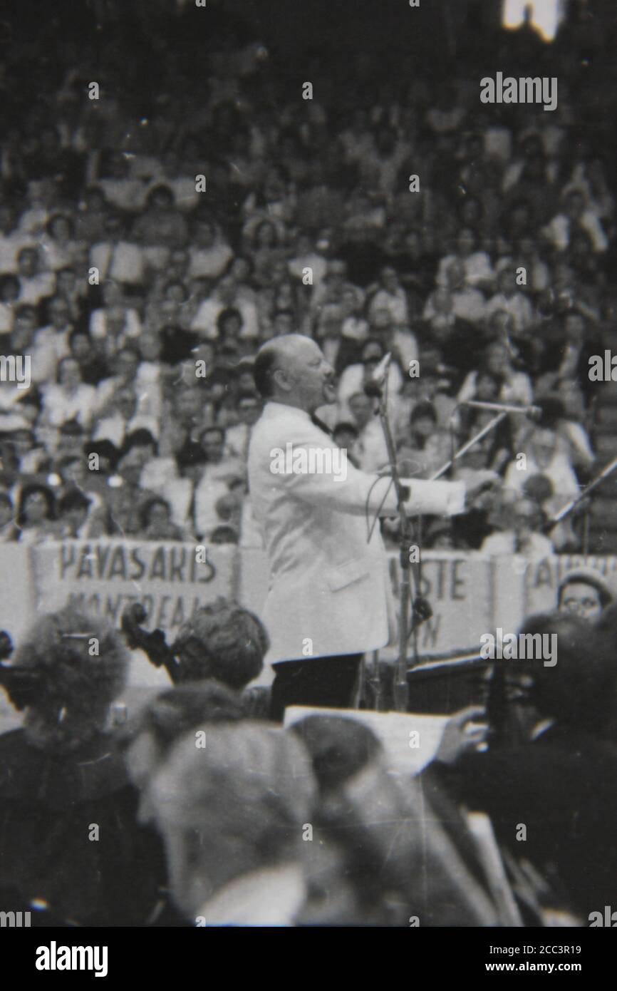 Fine 1970s vintage black and white photography of a conductor wearing a white tuxedo conducting an orchestra. Stock Photo