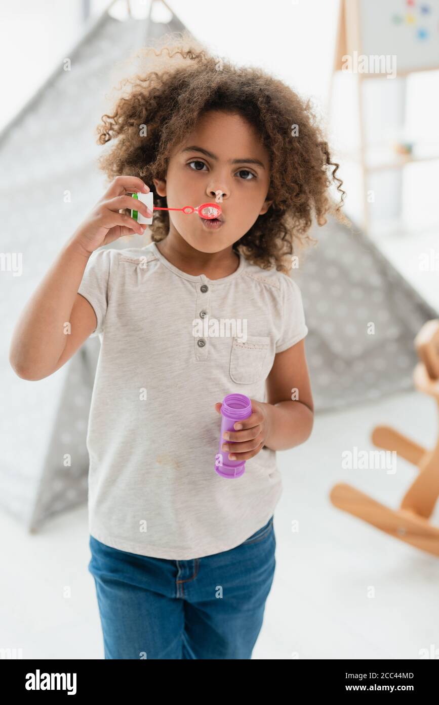 curly african american kid blowing soap bubbles and looking at camera Stock Photo