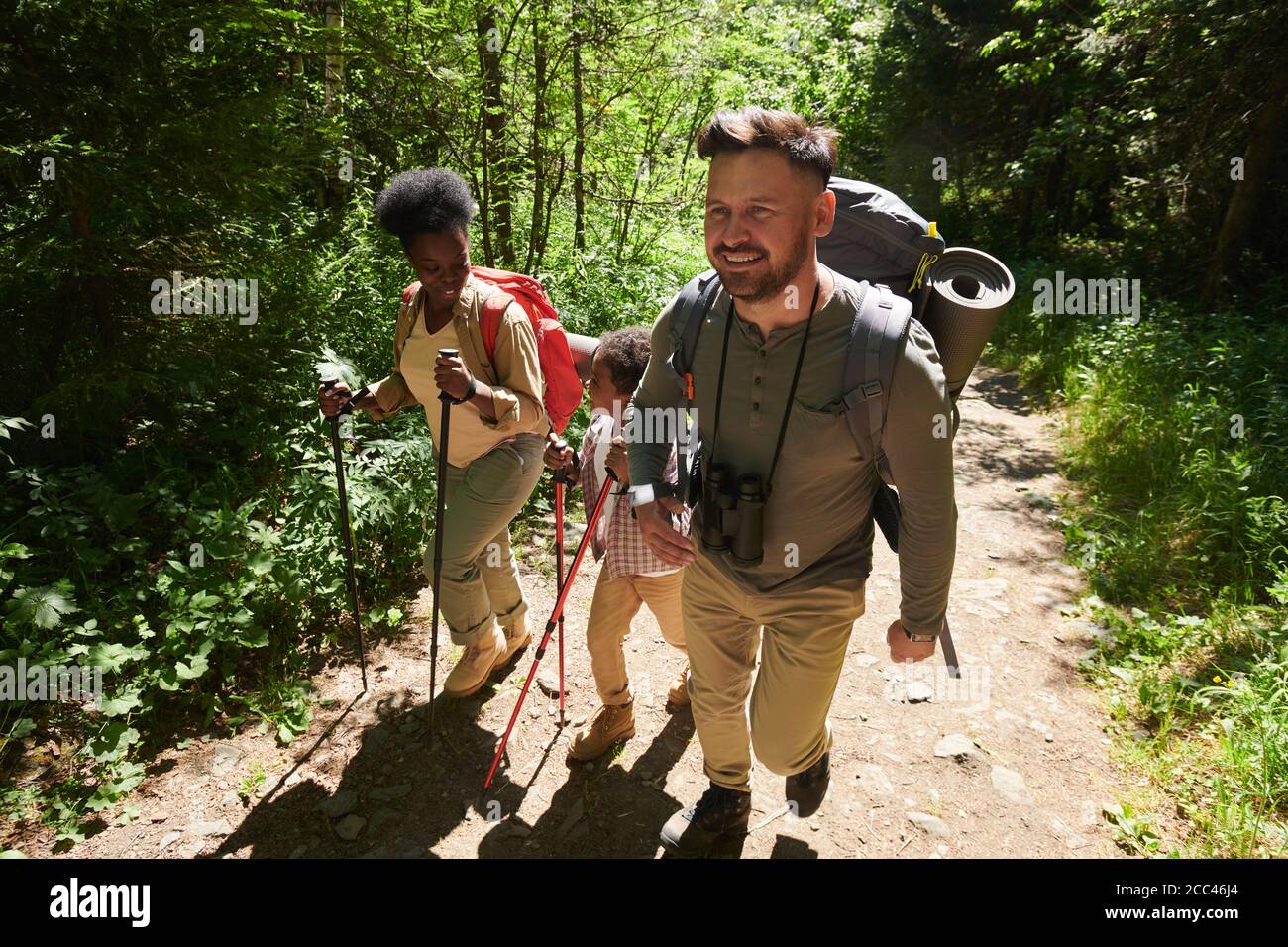 Man and woman with backpacks walking along the path in the forest together with their son they go camping Stock Photo