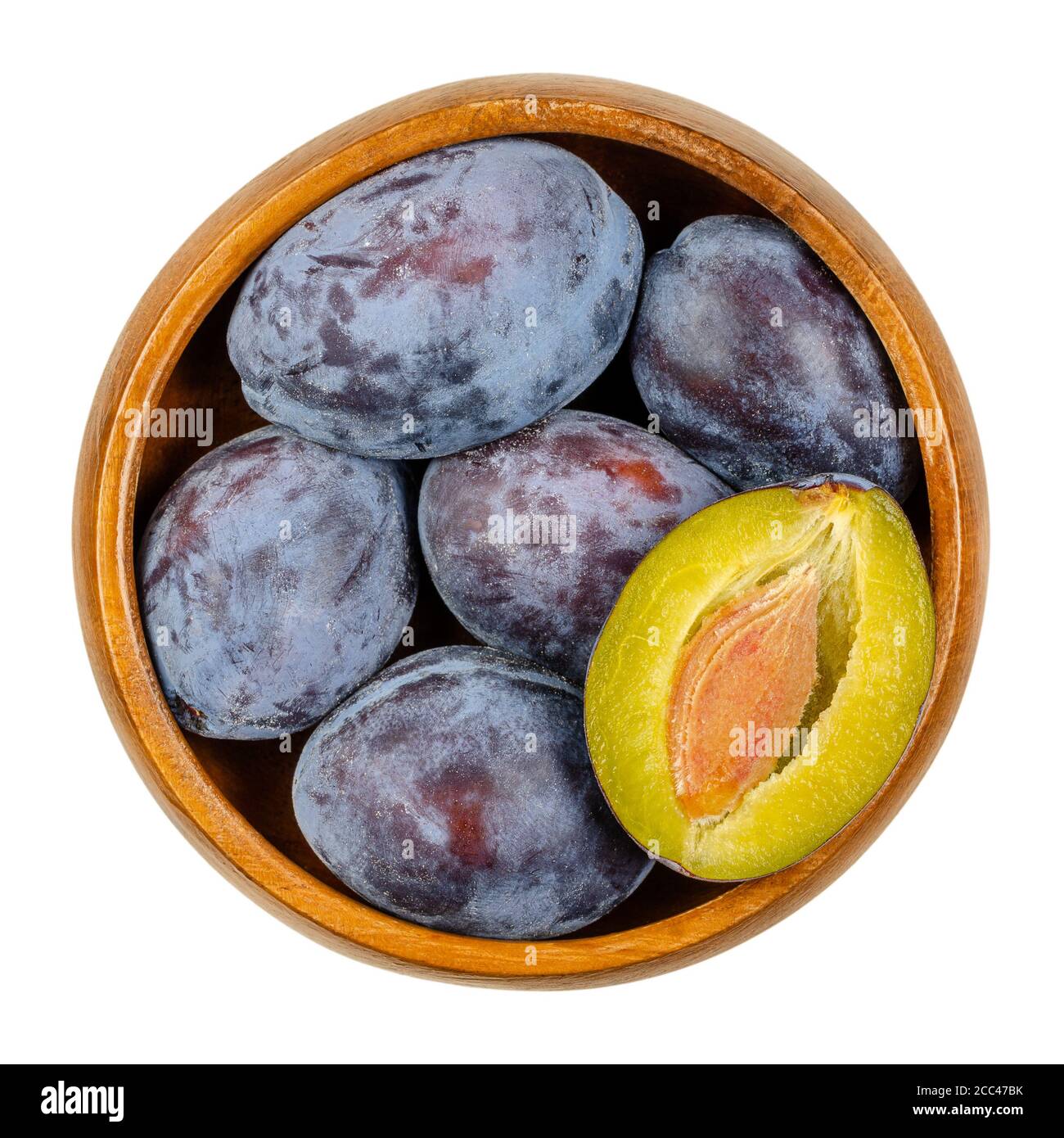 Ripe European plums with cross section of one fruit in a wooden bowl. Freestone fruit with purple, violet and black skin, also called Damson. Stock Photo