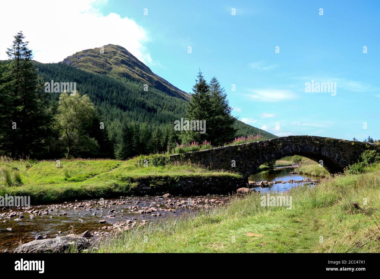 Ancient stone bridge spanning scottish a highland river with mountain behind Stock Photo