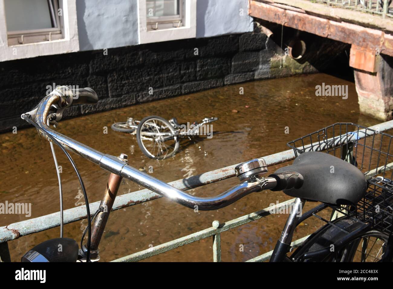 Leaned bicycle on metal railing of Freiburg water channel. In the running water is a skeleton of a bike severely damaged no more suitable for usage. Stock Photo