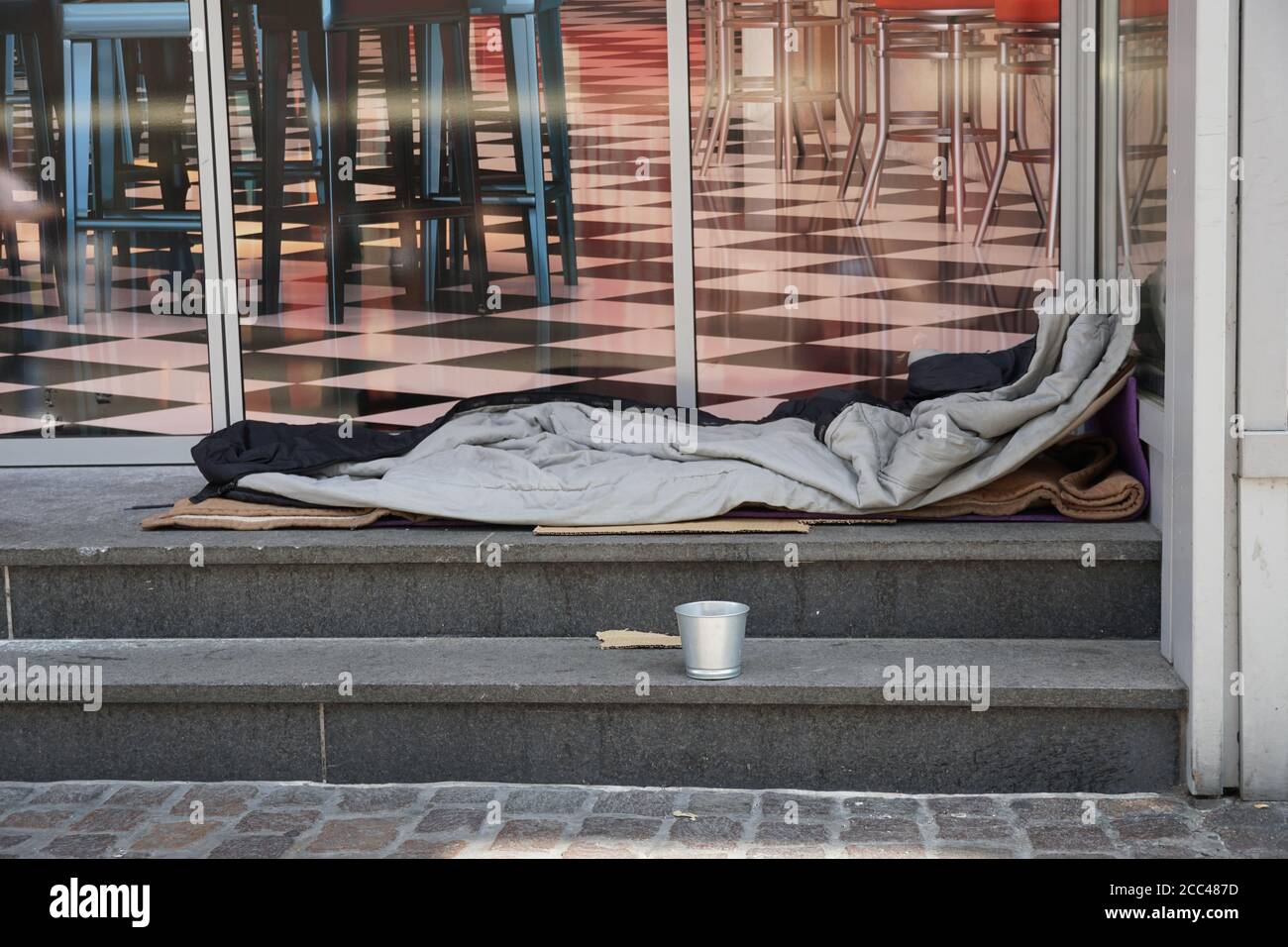 Sleeping bag of a homeless person spread on the stairs in front of a modern posh lounge or