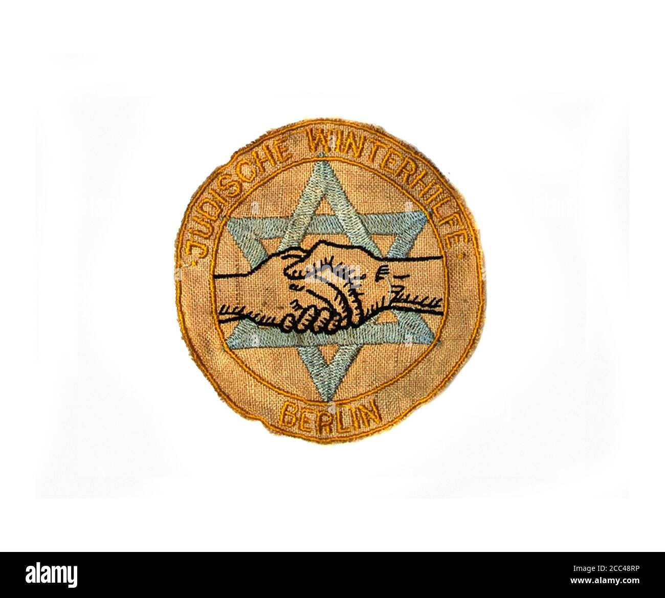 A German Jewish WWII winter aid patch. 'Judische Winterhilfe Berlin' cloth shoulder patch featuring two clasped hands before Star of David with the na Stock Photo
