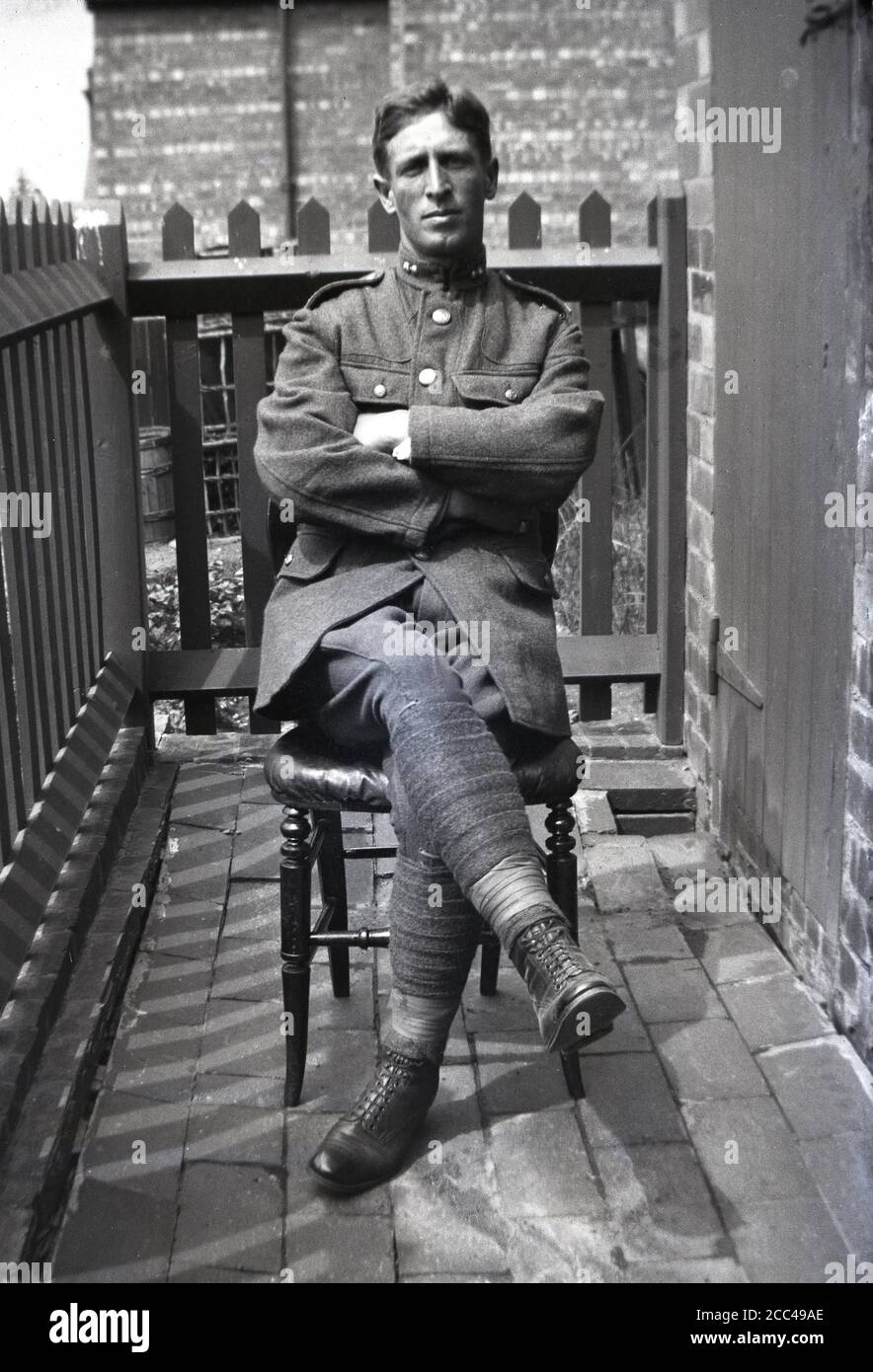 1916, historical, portrait of a British WW1 soldier in uniform, sitting on a chair outside on a narrow wooden balcony, England, UK. The British army Khaki uniforms were made from wool, with most soldiers, particularly the infantry, wearing puttees as seen here. These were cloth bands wound round a solider's leg from their anke to their knee, designed to provide support when walking, protection from hazards on the battefield and to prevent water getting into their boots in harsh weather conditions. They were also used in emergencies as a bandage. Stock Photo