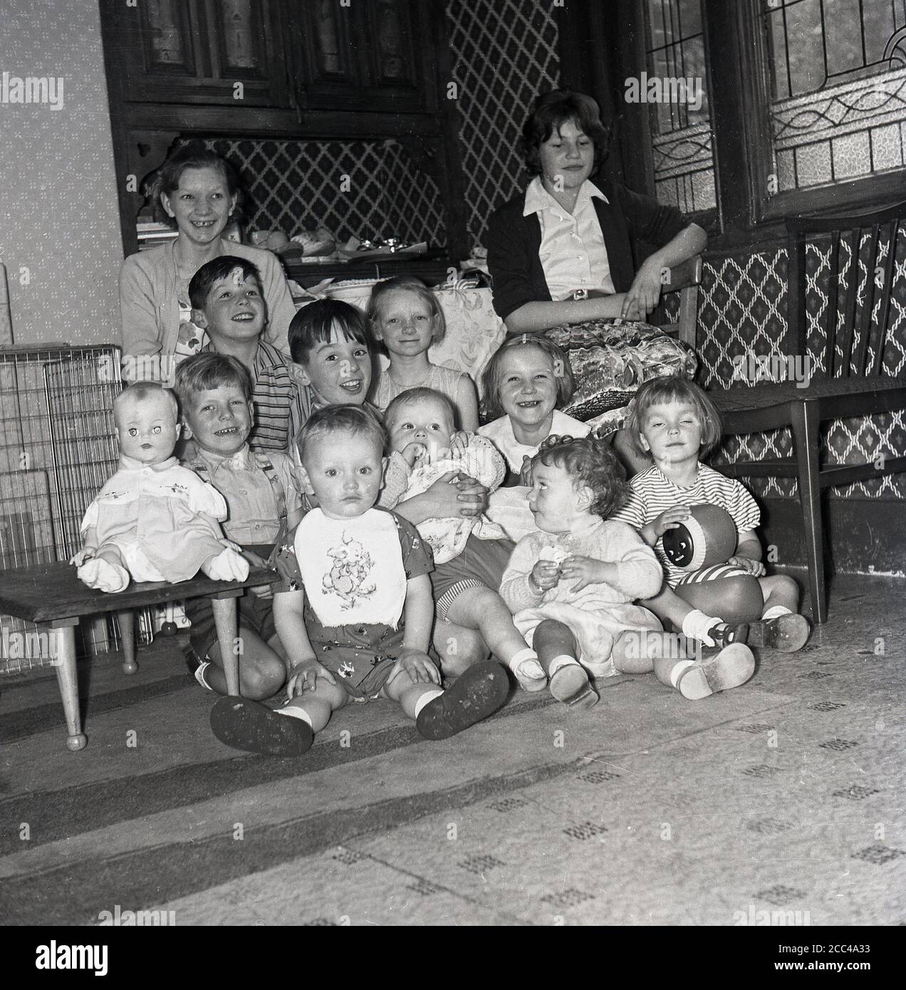 1950s, historical, group of scruffy but happy young and infant children sitting together in a  corner of a large room. Stock Photo