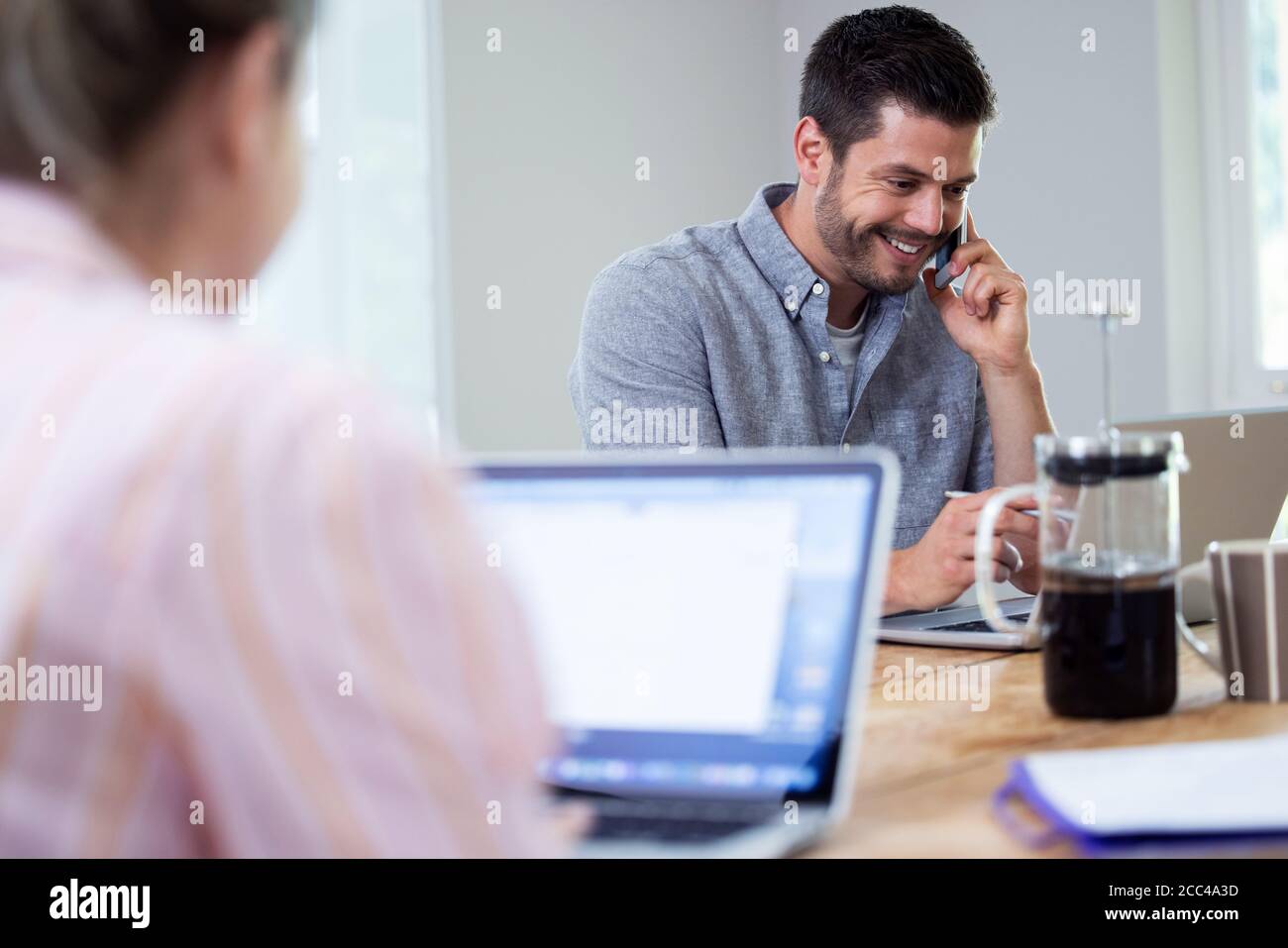Business Couple Working From Home Sitting At Table During Pandemic Lockdown Using Mobile Phone Stock Photo
