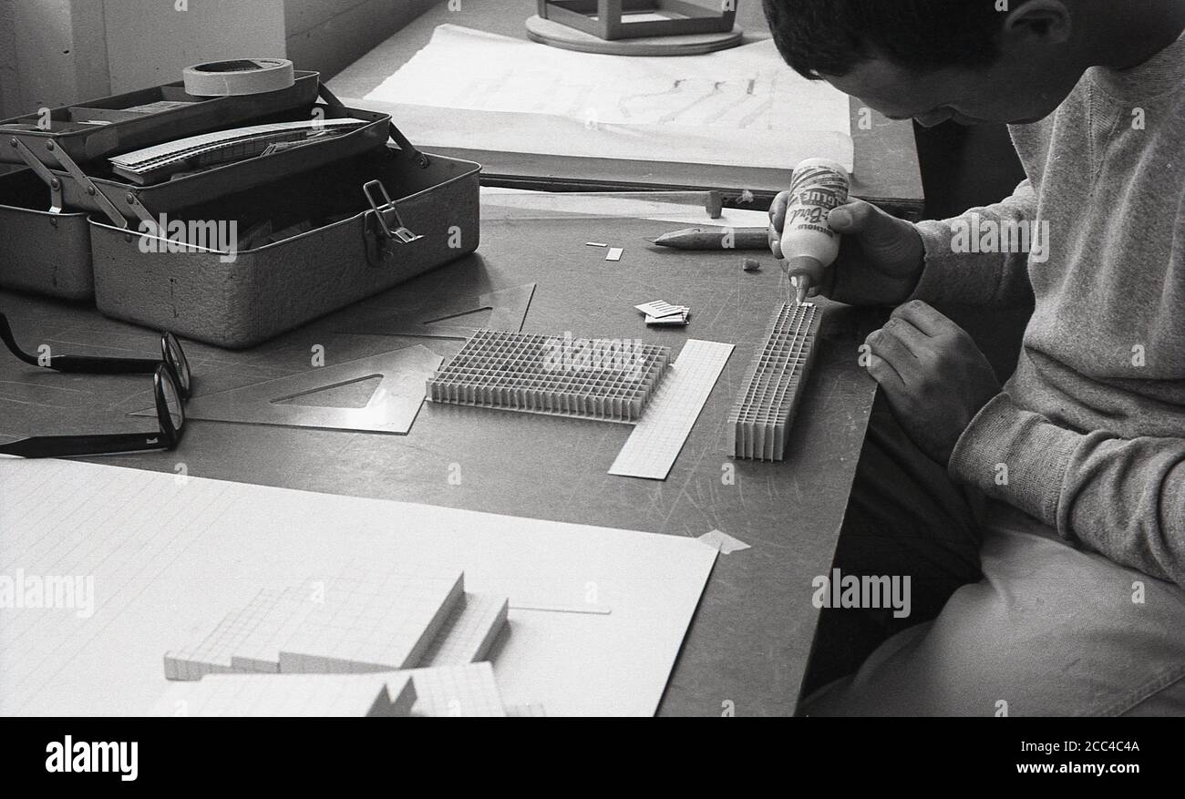 1964, historical, University architectural student sitting at a desk using a pot of glue to bond a paper together to make a model, California, USA. Stock Photo