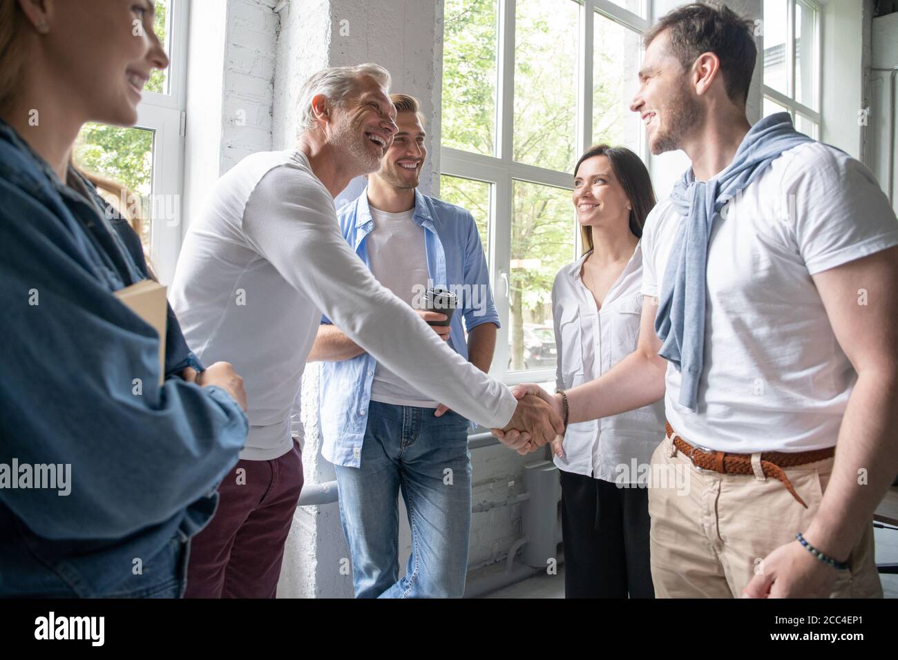 Welcome to our team! Business men in smart casual wear shaking hands while working in the creative office. Stock Photo
