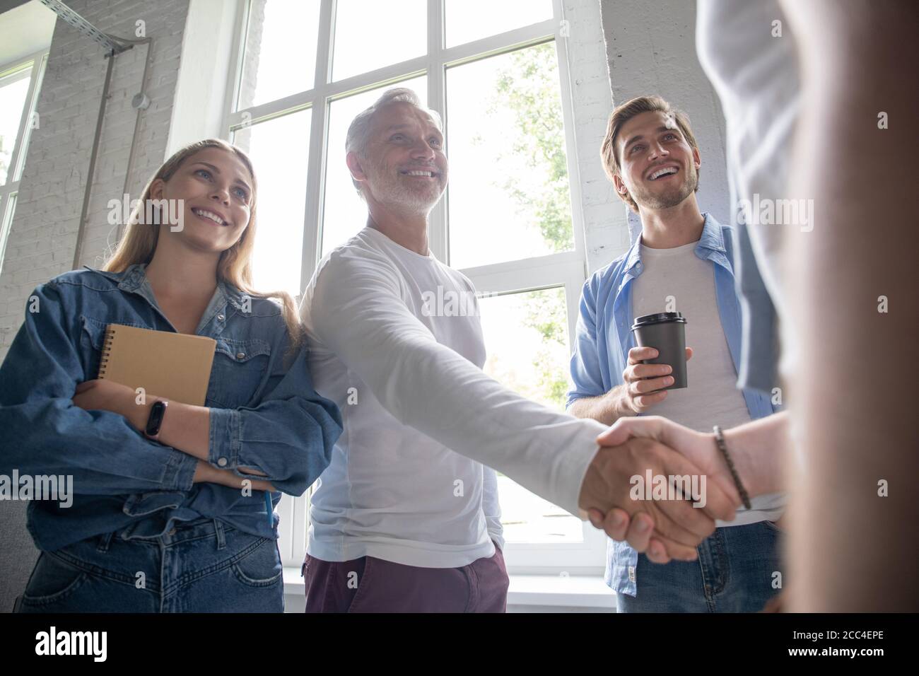 Welcome to our team! Business men in smart casual wear shaking hands while working in the creative office. Stock Photo