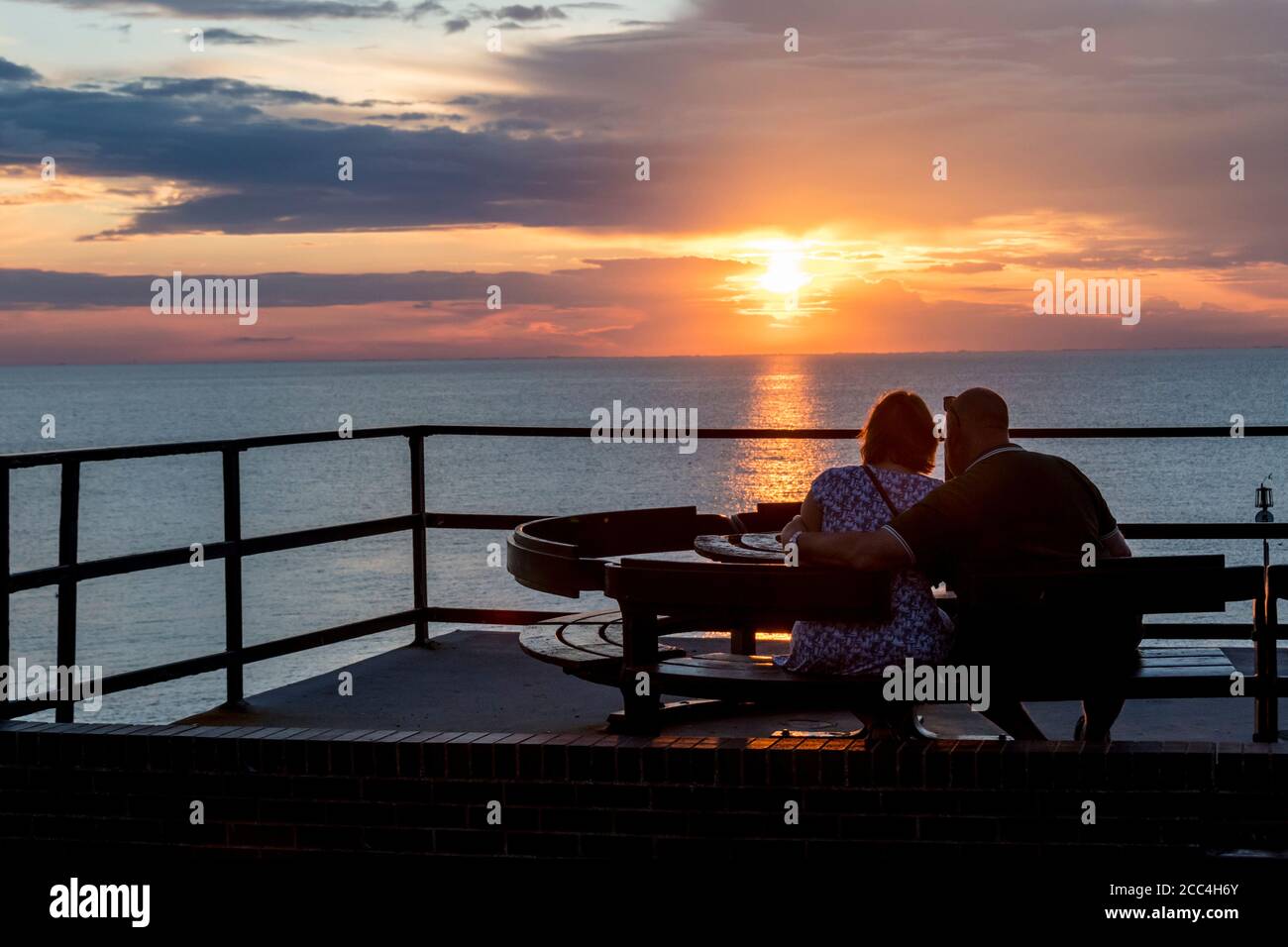 Couple watching the sun setting over the sea on the east coast at Hunstanton. Stock Photo