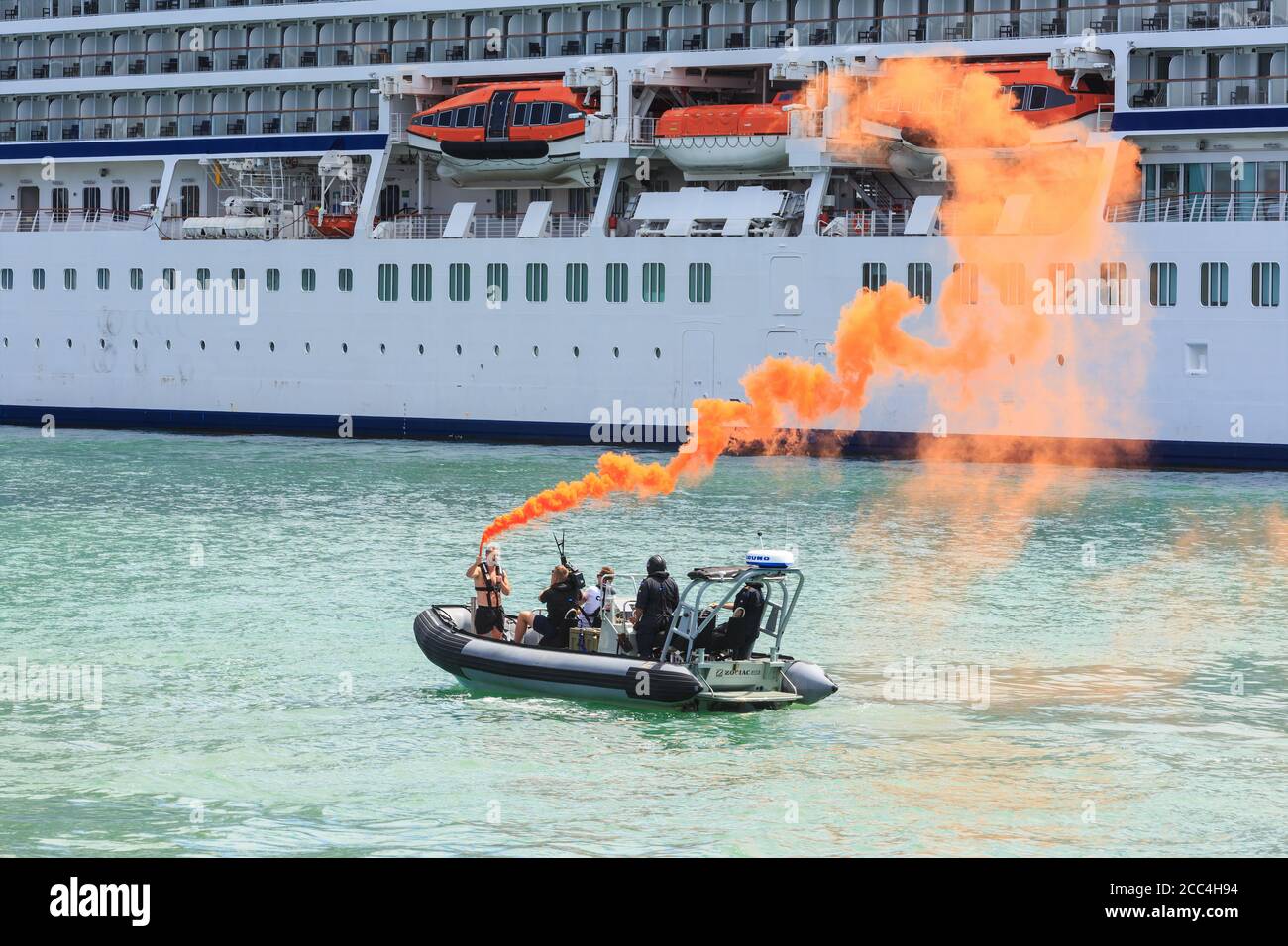 A man in an inflatable boat sets off a smoke flare in a simulated emergency. In the background is a cruise liner. Auckland, New Zealand, 1/25/2019 Stock Photo