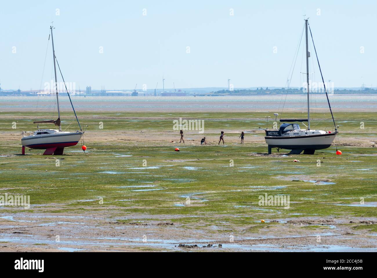 People and yachts out on the mud flats in Leigh on Sea, Essex, UK. At low tide the sea retreats a long way out and people walk out. Children playing Stock Photo