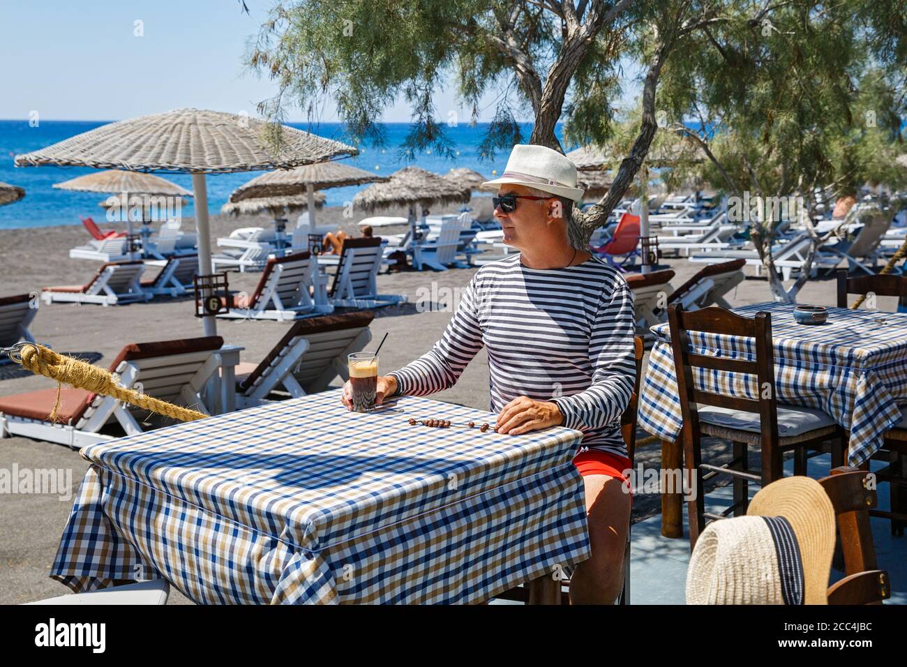 Man sits at a table at a beach cafe and drinks a cold drink Stock Photo ...