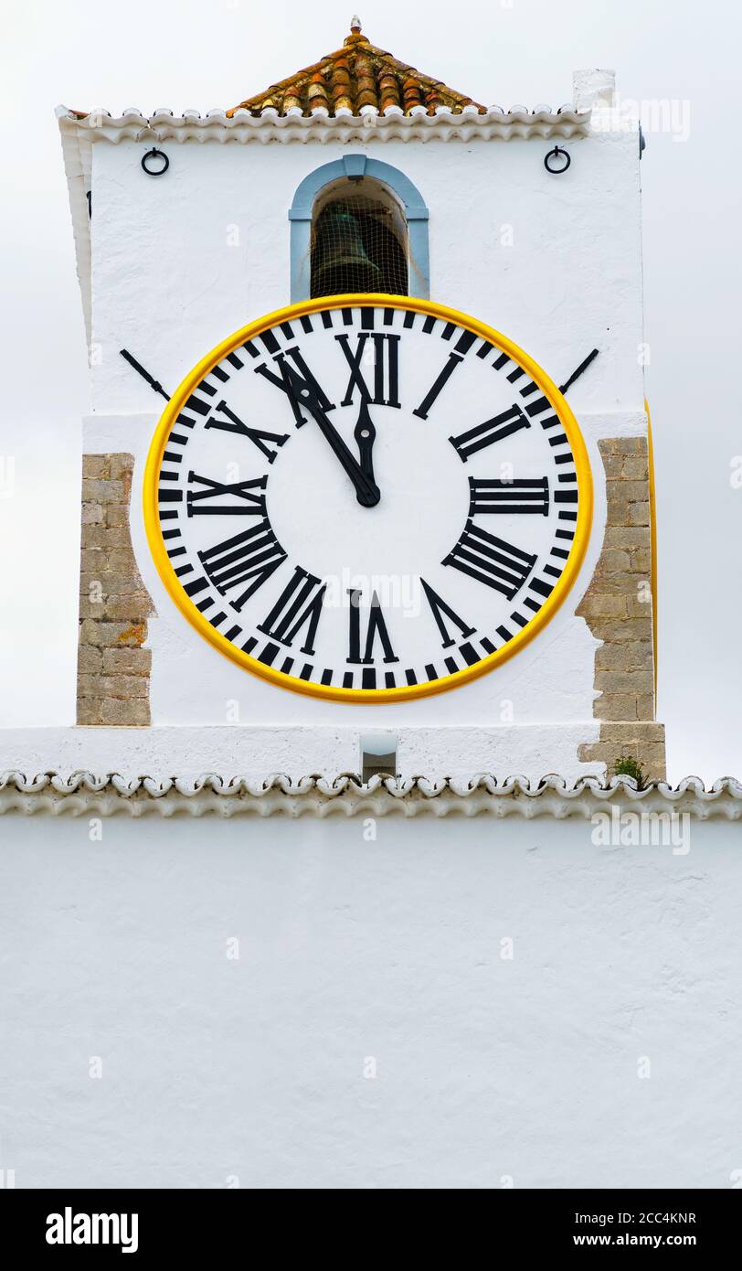 Church clock of a white mediterranean church with roman numerals. Hands showing five minutes to twelve. Time pressure, deadline, urgency, appointment Stock Photo